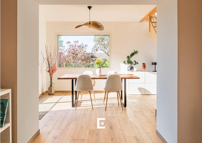 Vue depuis la maison d’origine sur une ouverture menant à un salon baigné de lumière naturelle.