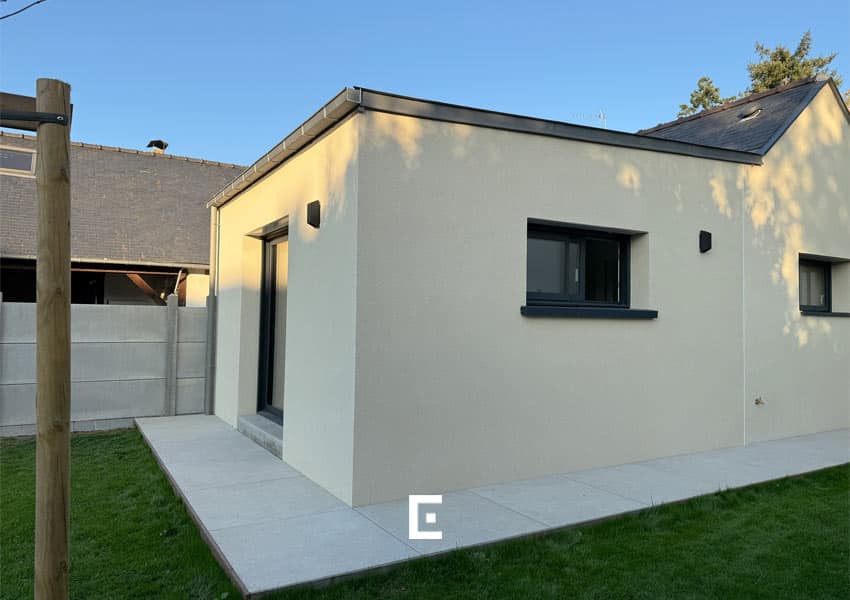 Extension réalisée en parpaing avec enduit, toiture en zinc et menuiseries aluminium, pour un ensemble sobre et moderne.