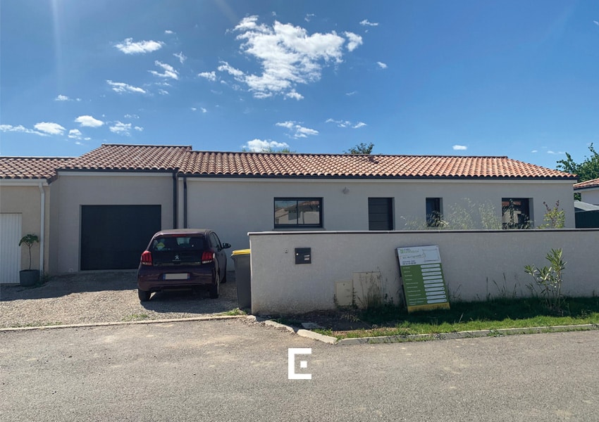 Maison blanche de plain-pied avec toiture en ardoise, extension garage avec porte noire électrique, et voiture garée devant, dans un lotissement de maisons accolées.