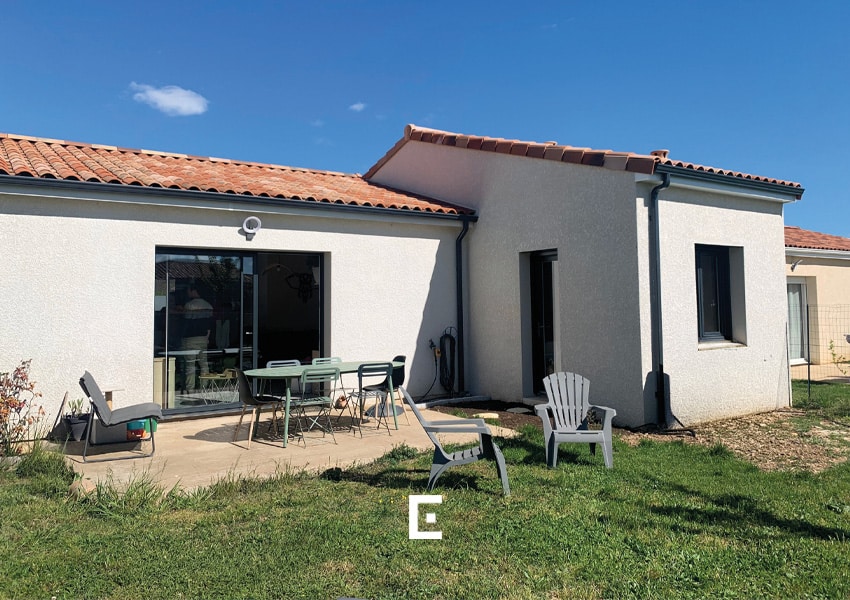 Terrasse aménagée avec salon de jardin et espace détente sur pelouse à l'arrière d'une maison.