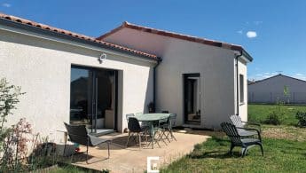 Terrasse aménagée avec salon de jardin et espace détente sur pelouse à l'arrière d'une maison.