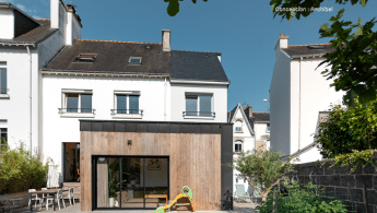 Vue d’une maison avec son extension contemporaine, entourée d’un jardin verdoyant et dotée d’une porte d’entrée en bois, à Lorient.