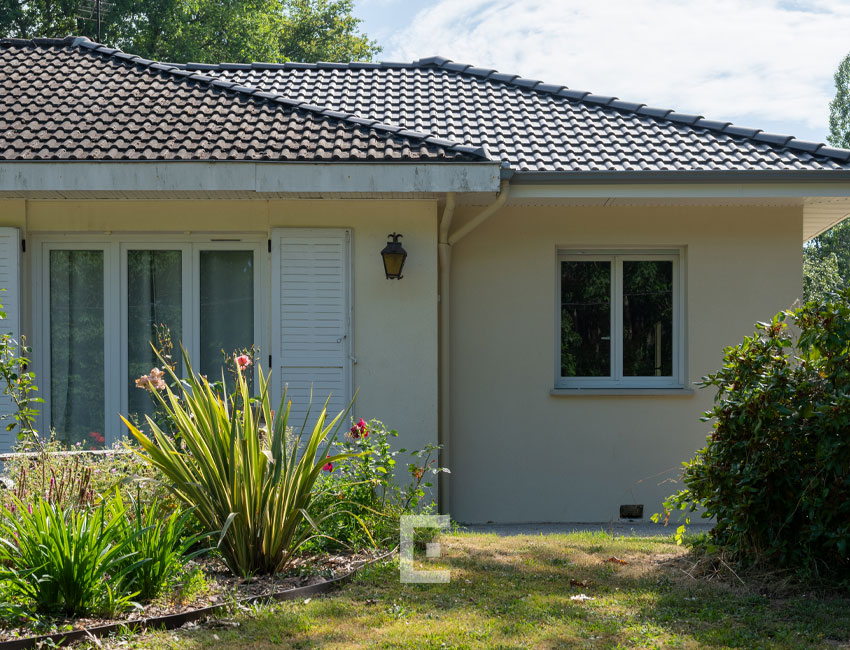 Zoom sur la fenêtre PVC blanche de l’extension maçonnée à côté des volets de la maison existante.