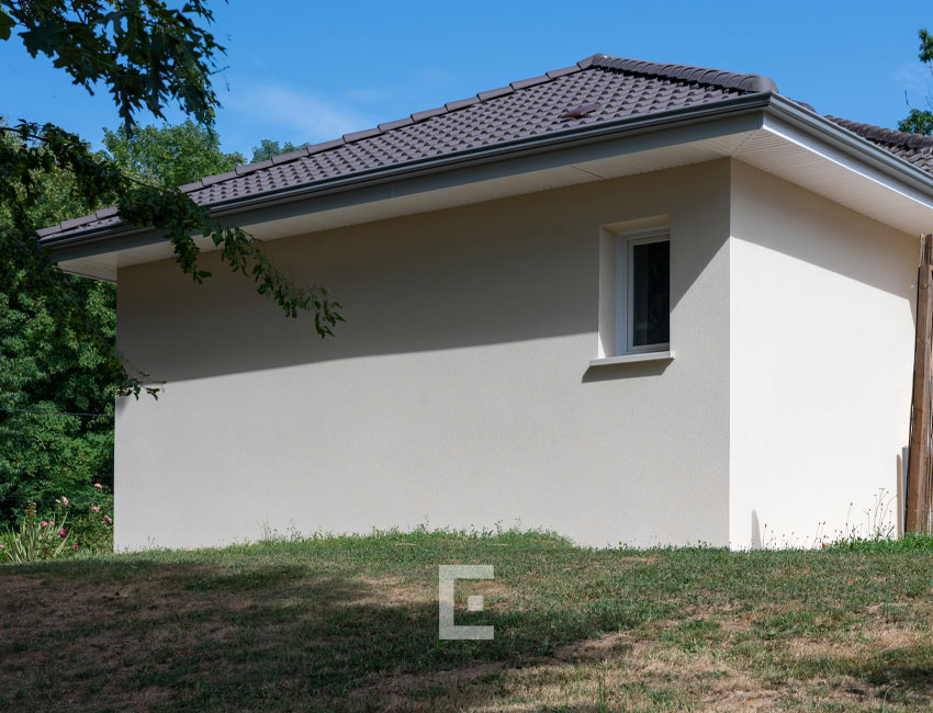 Angle arrière d’une extension de maison maçonnée avec mur crépi beige et petite fenêtre carrée.