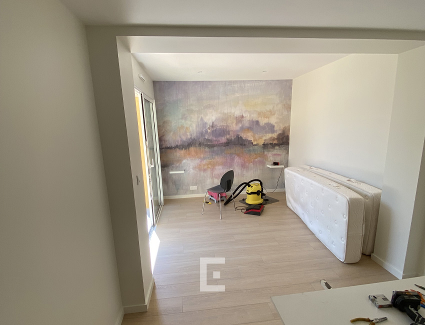 Pièce de vie de l’extension avec sol imitation bois clair, grande baie vitrée et mur décoré d’un paysage abstrait.