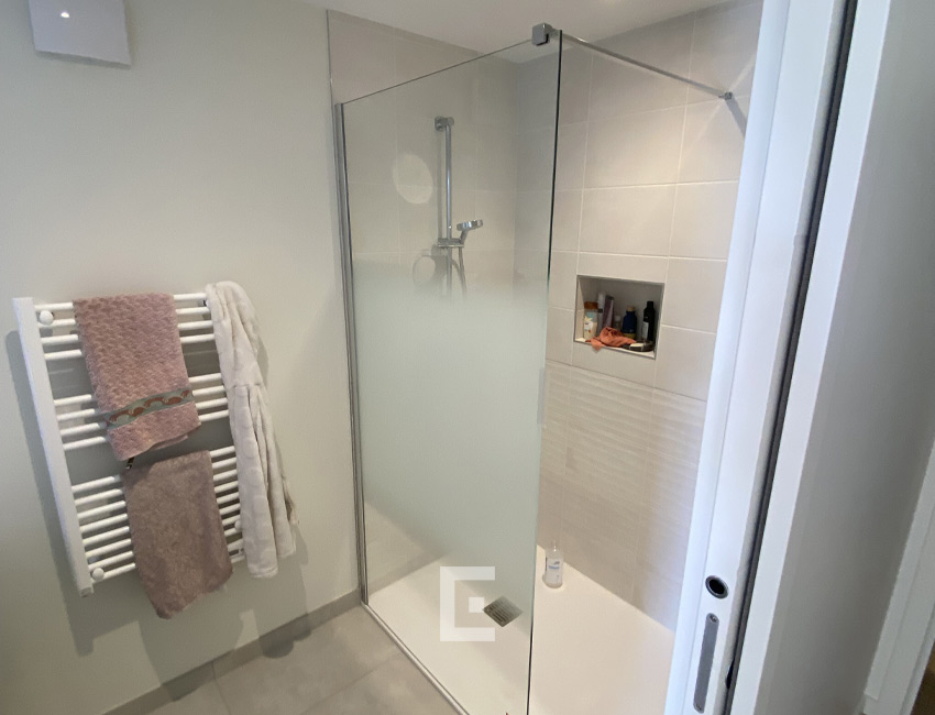 Douche avec receveur blanc, paroi vitrée transparente, robinetterie chromée et niche murale intégrée.