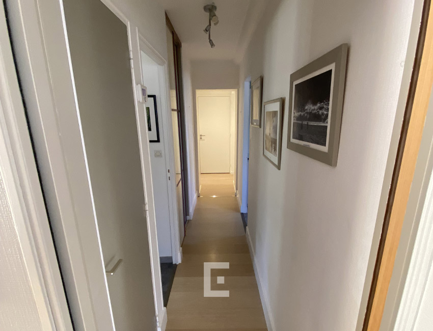 Couloir intérieur aux murs blancs, sol beige clair et portes donnant accès aux différentes pièces de la maison.